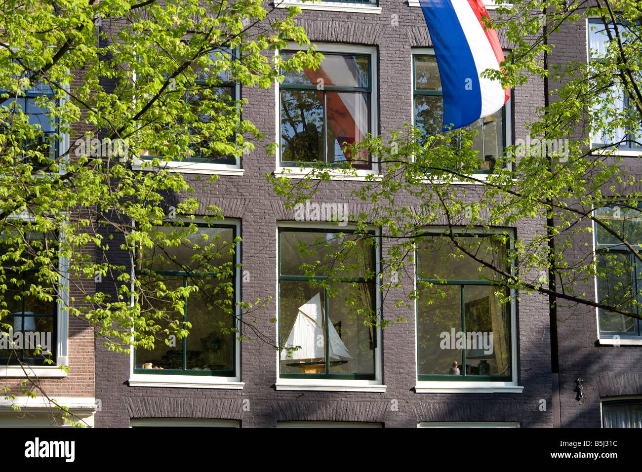 Amsterdam. Maison sur un canal dans le quartier Jordaan avec drapeau national néerlandais et un modèle voile de bateau sur le rebord. Le printemps. Banque D'Images