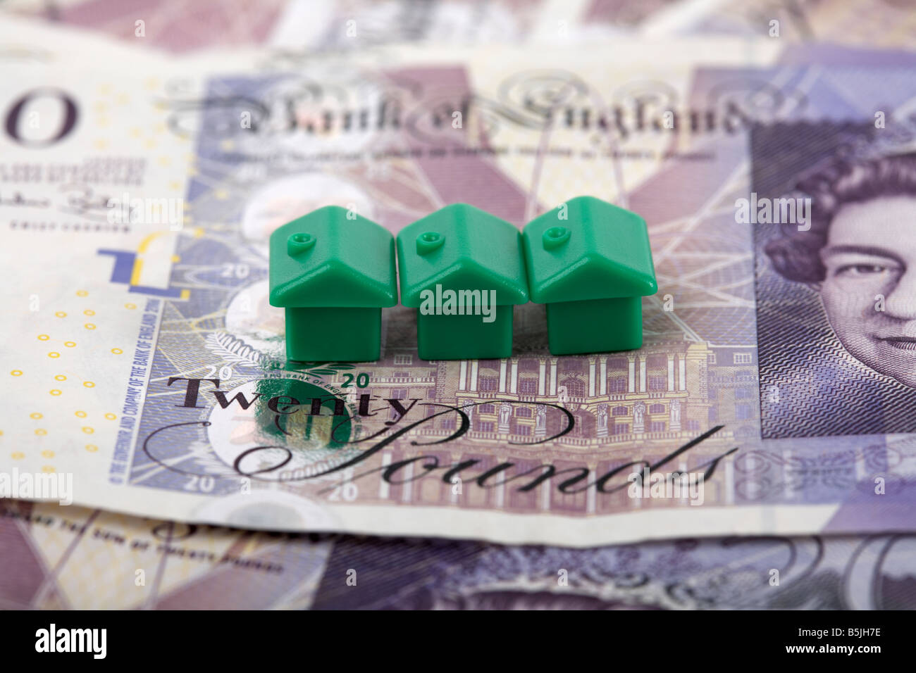 Trois maisons vertes sur le dessus d'une pile de 20 livres sterling en espèces de billets de banque Banque D'Images