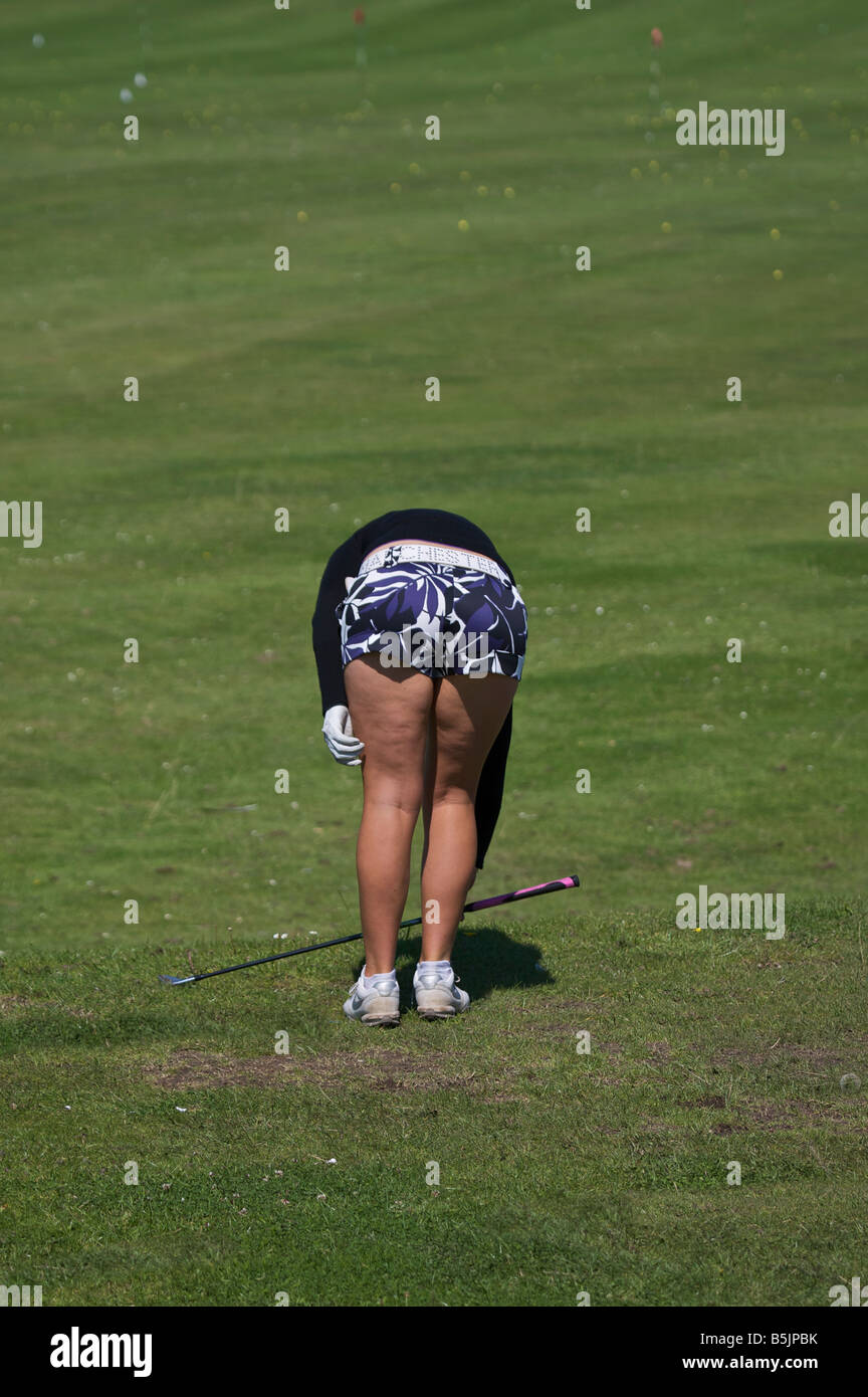 Golfeur Dame en se penchant pour prendre un club de golf montrant le côté ludique du golf Banque D'Images