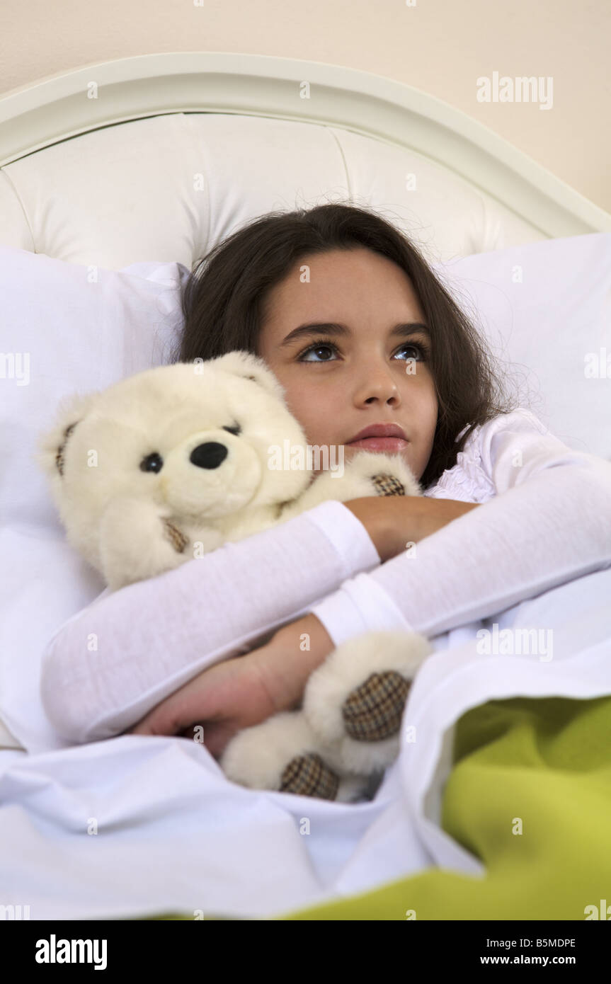 Une petite fille dans le lit avec un ours en peluche Banque D'Images