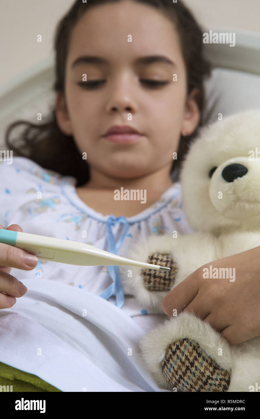 Une petite fille dans le lit à la recherche d'un thermomètre à Banque D'Images
