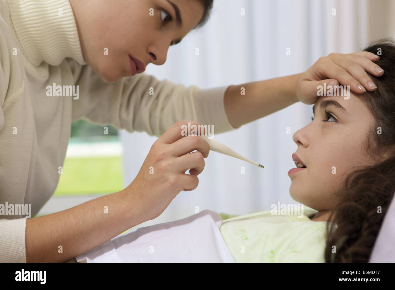 Une petite fille obtenir un thermomètre placé dans la bouche par une femme Banque D'Images