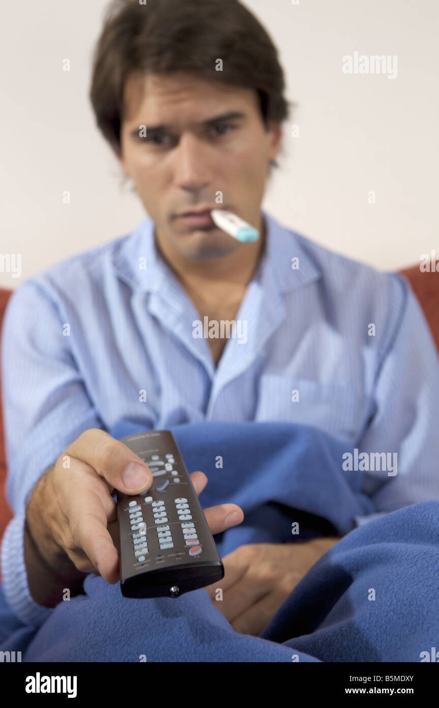 Un homme avec un thermomètre dans la bouche et la tenue d'un contrôle à distance Banque D'Images