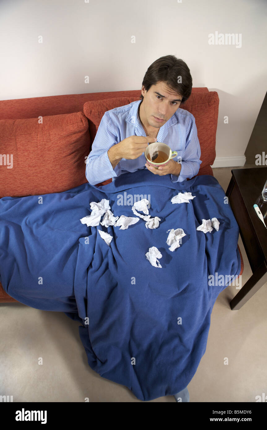 Un homme malade assis sur un canapé avec une tasse de thé Banque D'Images