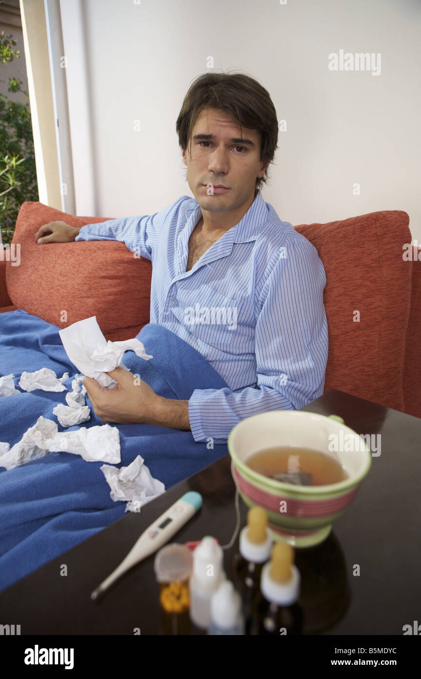 Un homme malade wearing pajamas while sitting on a couch Banque D'Images