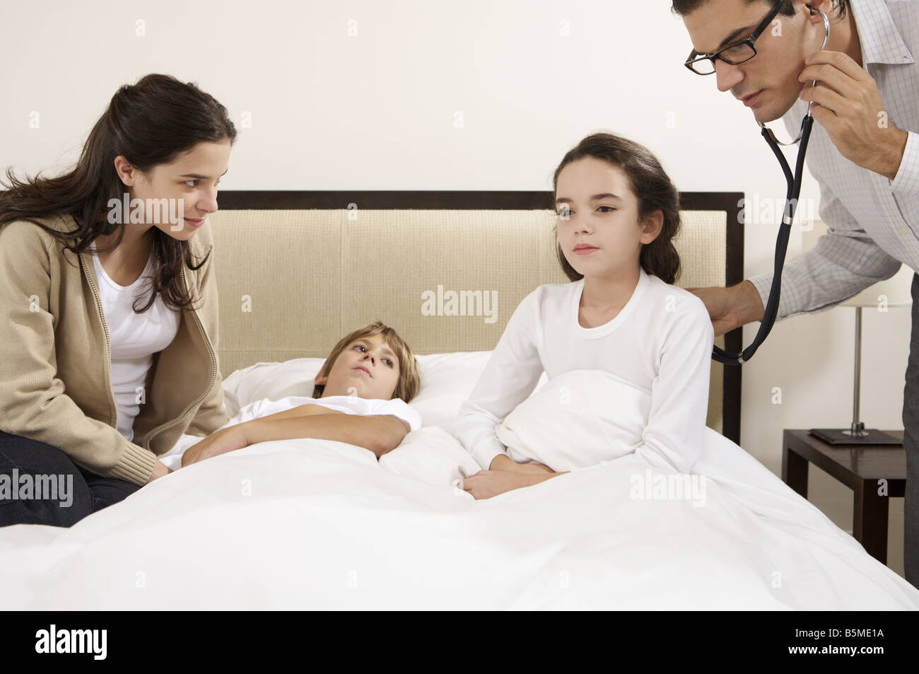 Un médecin l'examen de deux enfants au lit Banque D'Images