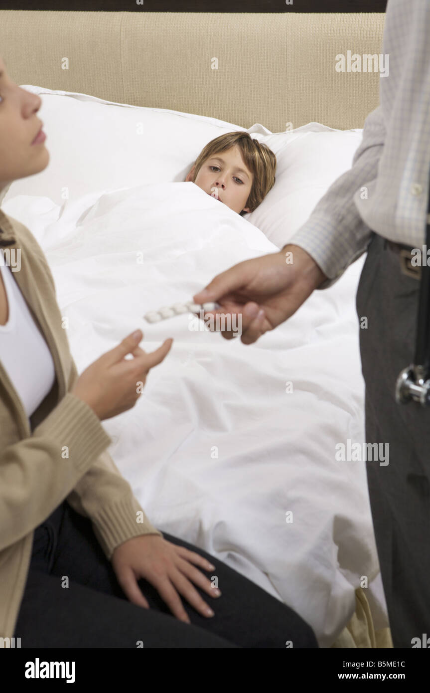 Une femme assise sur un lit du garçon alors qu'un homme lui donne une plaquette de pilules Banque D'Images