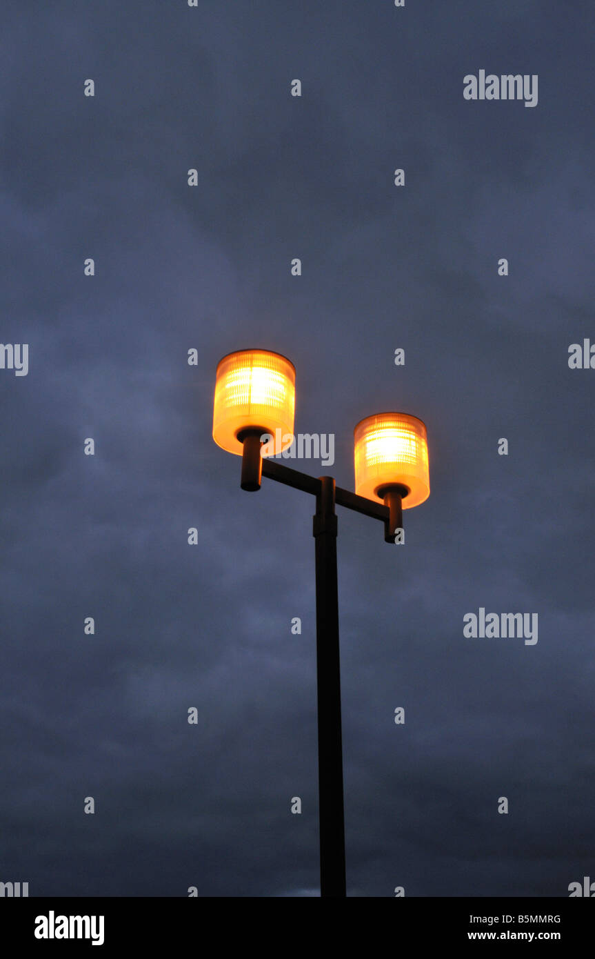 Eerie spectaculaire terrain de stationnement lampes glow au crépuscule contre gris bleu ciel nuageux Banque D'Images