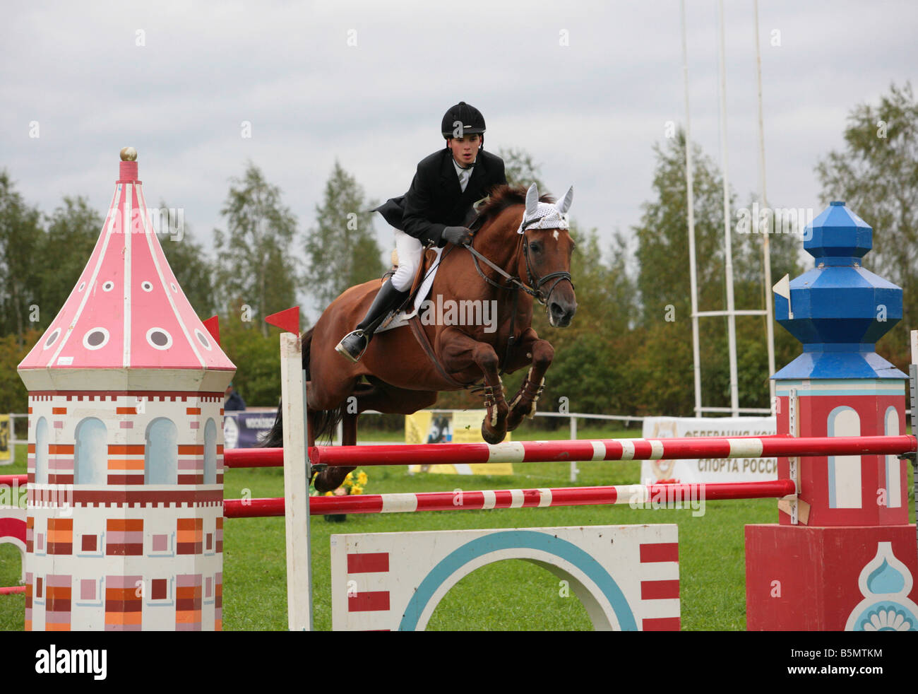 Cavalier équestres pris dans le milieu de sauter avec l'herbe et des clôtures blanches dans l'arrière-plan Banque D'Images