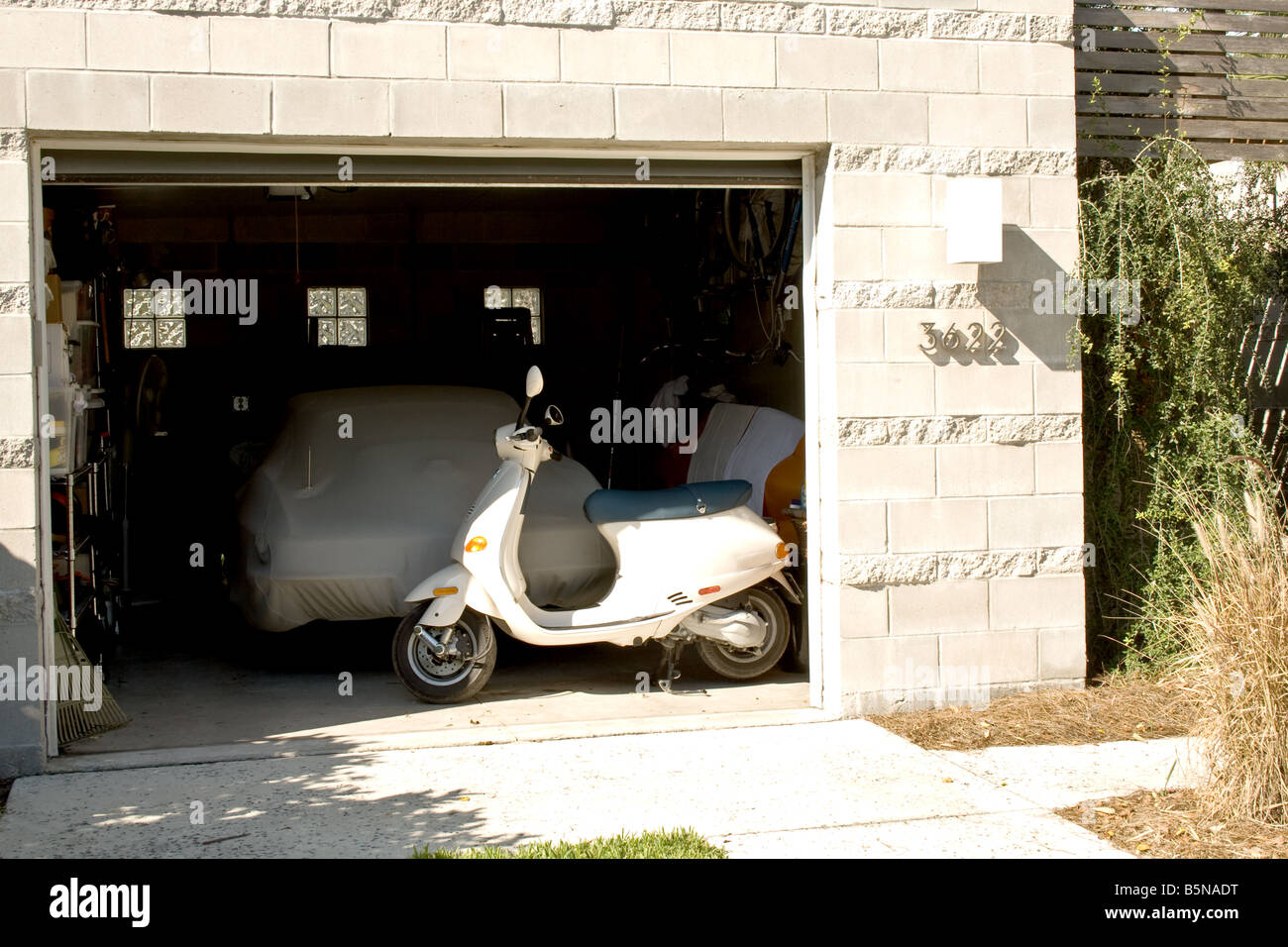 Photo de scooter devant une voiture recouverte d'une bâche de toile dans un garage Banque D'Images