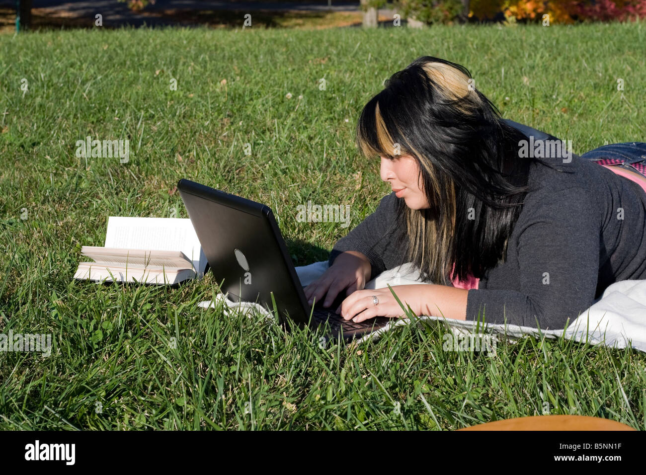 Un jeune étudiant en utilisant son ordinateur portable tout en jetant dans l'herbe par une belle journée Banque D'Images
