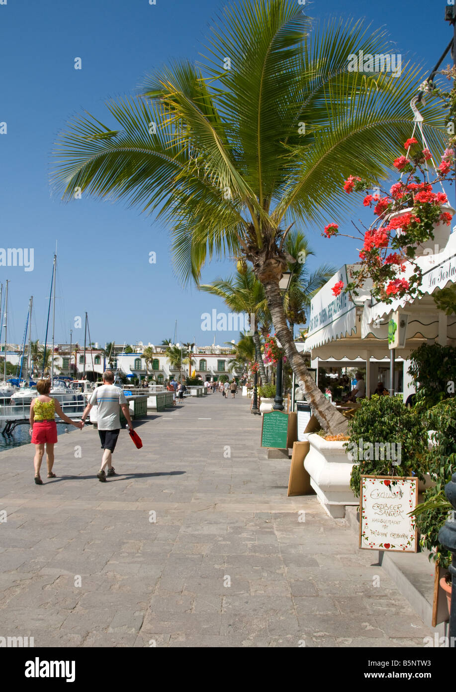 Puerto de Mogán Couple promenade le long de la promenade de Marina au bord de l'eau colorée avec des restaurants de Puerto de Mogan Gran Canaria Îles Canaries Espagne Banque D'Images