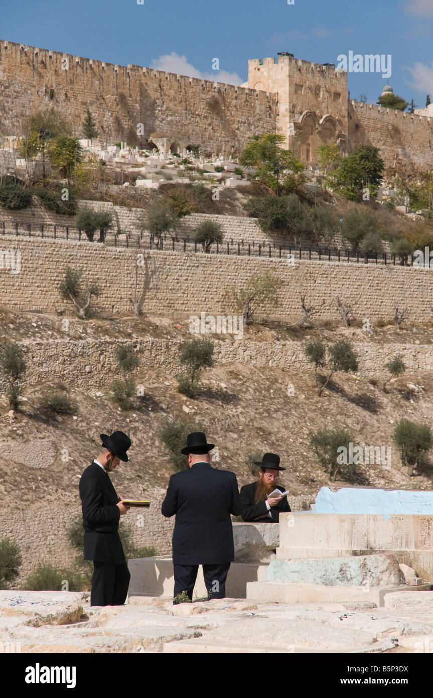 Mont des Oliviers Jérusalem Israël trois juifs orthodoxes priant à un tombeau avec Golden Gate de bkgd Banque D'Images