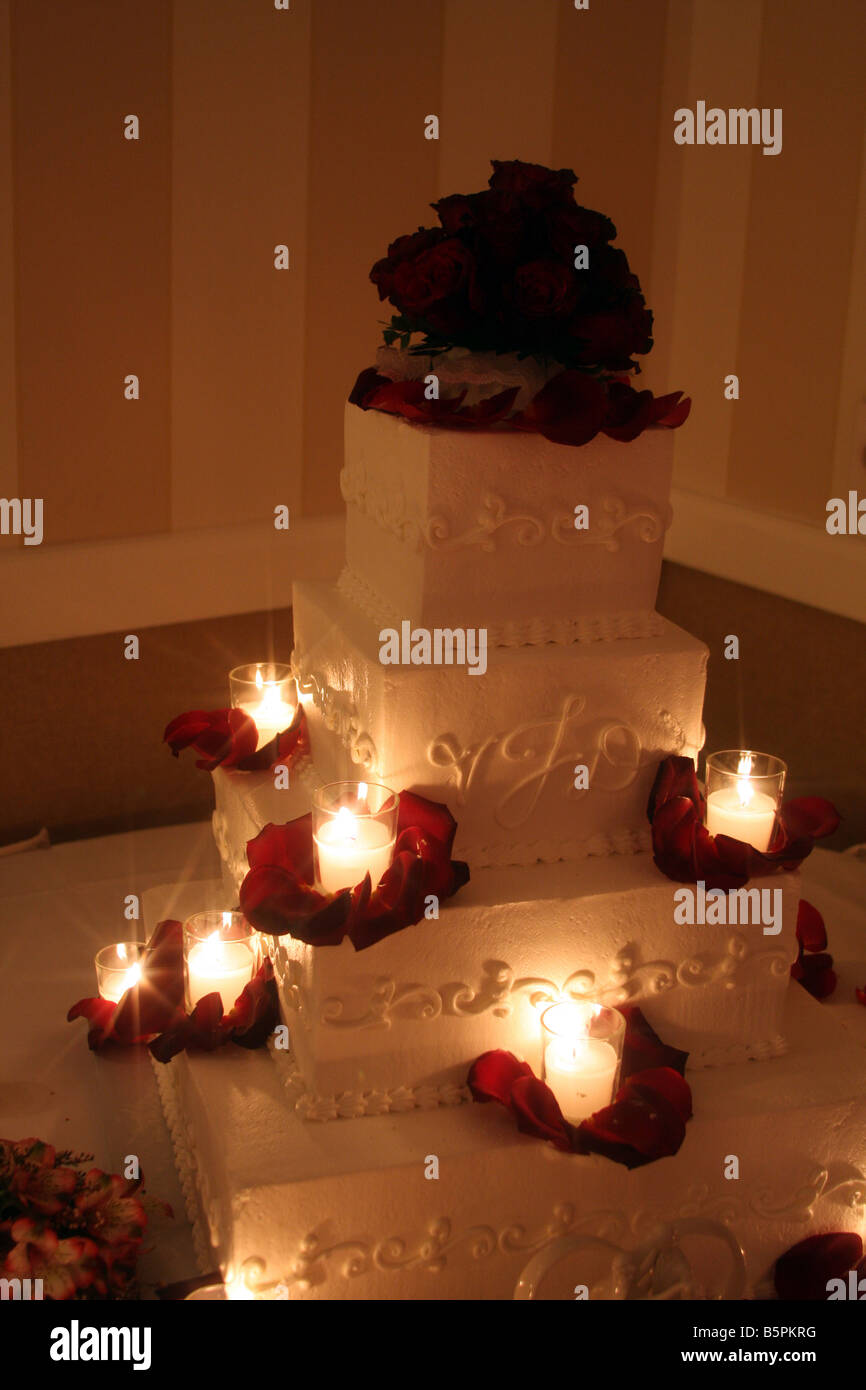 Un beau gâteau de mariage avec des roses rouges sur le dessus et des bougies allumées autour du cake affiché pour une réception de mariage Banque D'Images