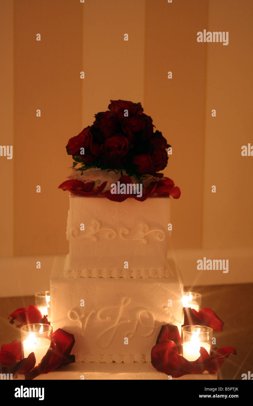 Un beau gâteau de mariage avec des roses rouges sur le dessus et des bougies allumées autour du cake affiché pour une réception de mariage Banque D'Images