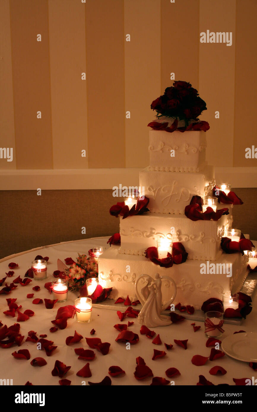 Un beau gâteau de mariage avec des roses rouges sur le dessus et des bougies allumées autour du cake affiché pour une réception de mariage Banque D'Images