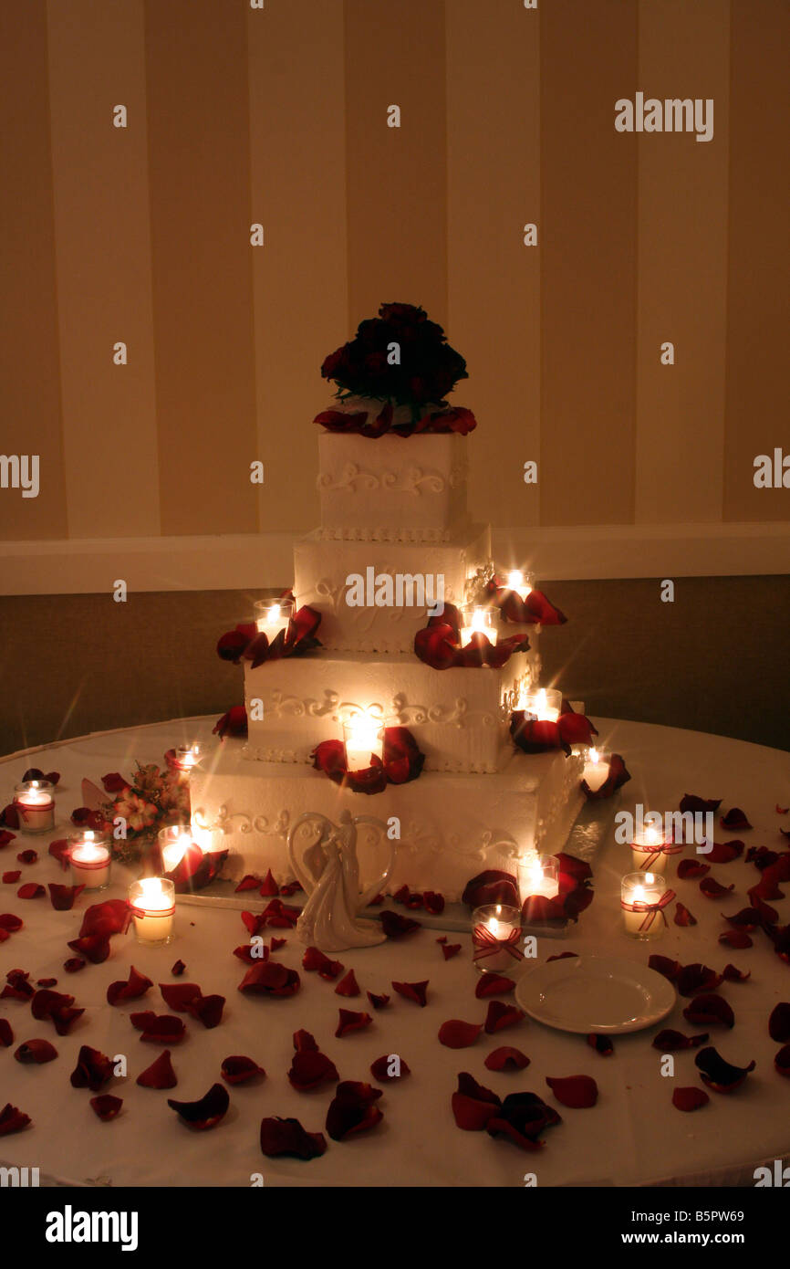 Un beau gâteau de mariage avec des roses rouges sur le dessus et des bougies allumées autour du cake affiché pour une réception de mariage Banque D'Images