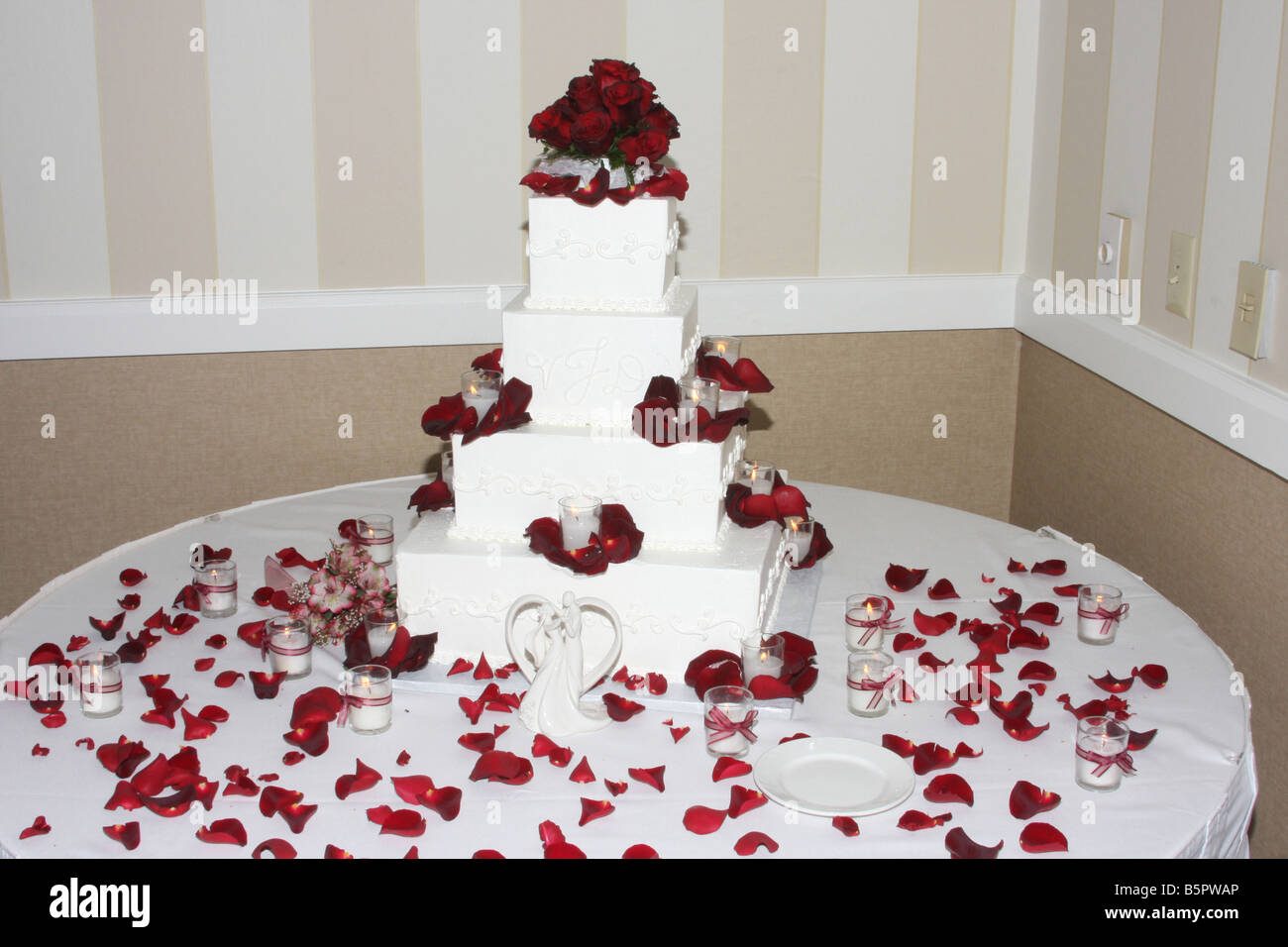 Un beau gâteau de mariage avec des roses rouges sur le dessus et des bougies allumées autour du cake affiché pour une réception de mariage Banque D'Images