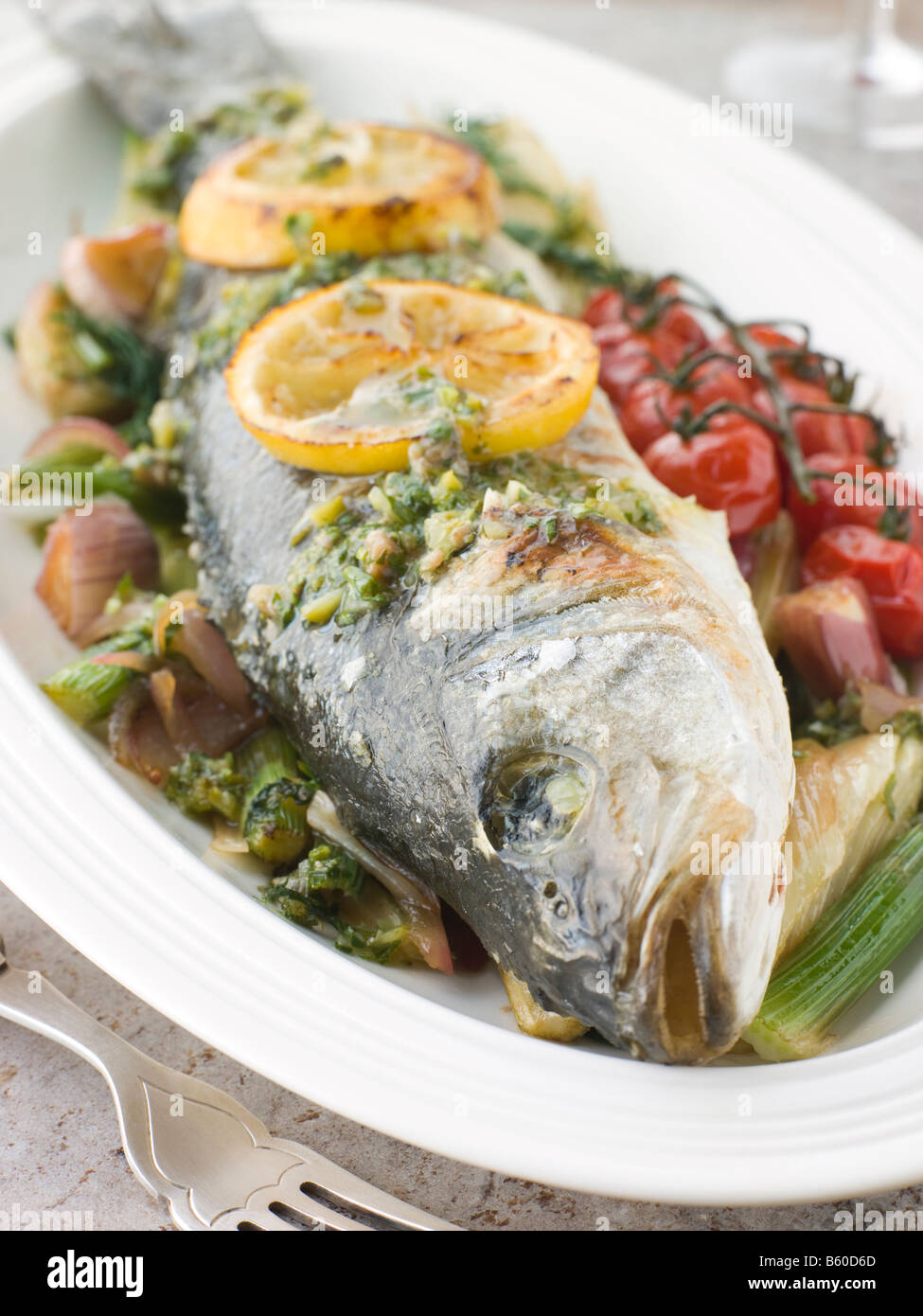 Loup de mer rôti entier avec des tomates cerise Citron Fenouil et salsa verde Banque D'Images