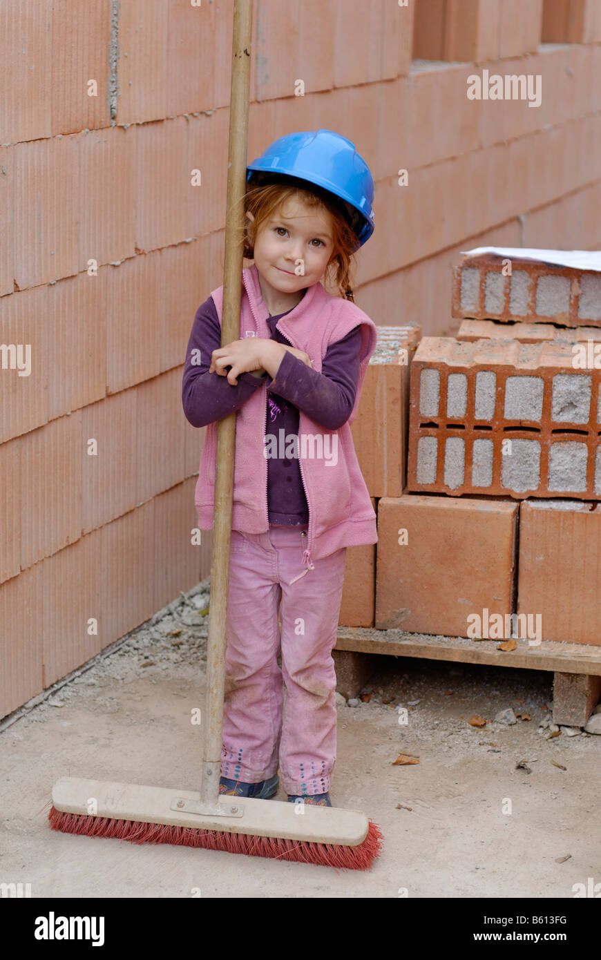 Little girl holding a broom et portant un casque bleu à une maison construction site Banque D'Images