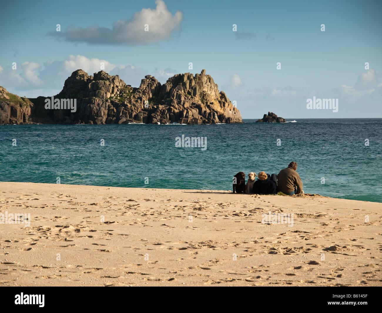 Couple assis sur plage de Porthcurno, avec Logan's Rock dans l'arrière-plan Banque D'Images