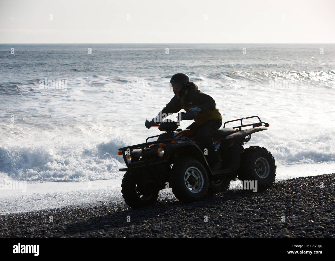 Girl riding Quad sur sable noir plage rocheuse, Hornafjordur, fjord Islande de l'Est Banque D'Images