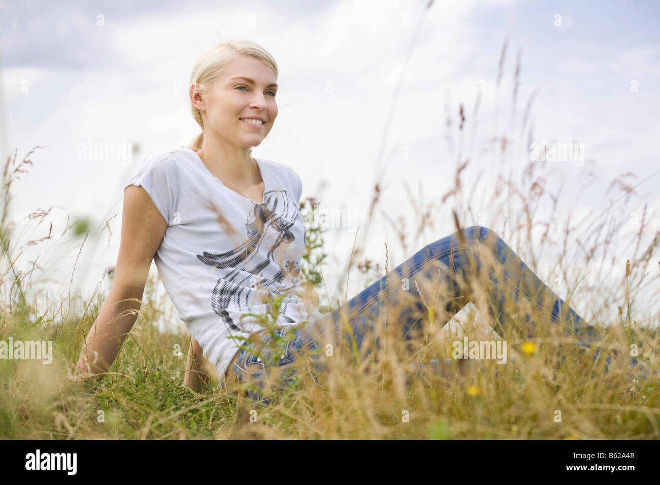 Jeune femme blonde assise dans l'herbe haute Banque D'Images