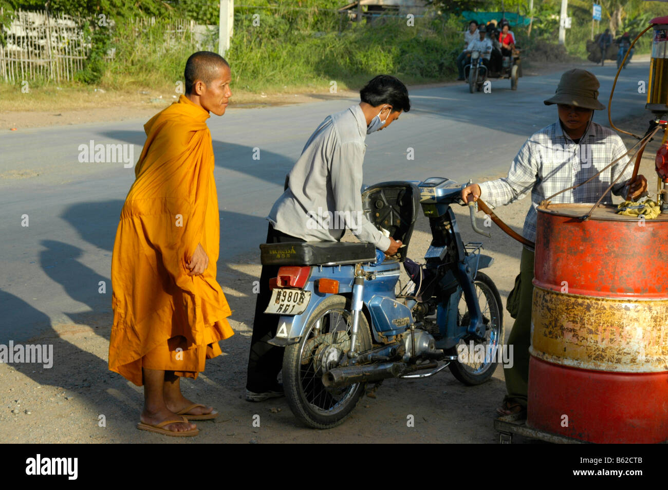 Pilote de moto avec un moine à une station essence primitive, près de Phnom Penh, au Cambodge, en Asie du sud-est Banque D'Images