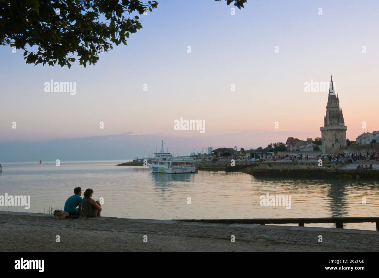 Couple assis à l'entrée du port au crépuscule, en face de l'ancienne tour de la prison La Rochelle Charente Maritime France Banque D'Images