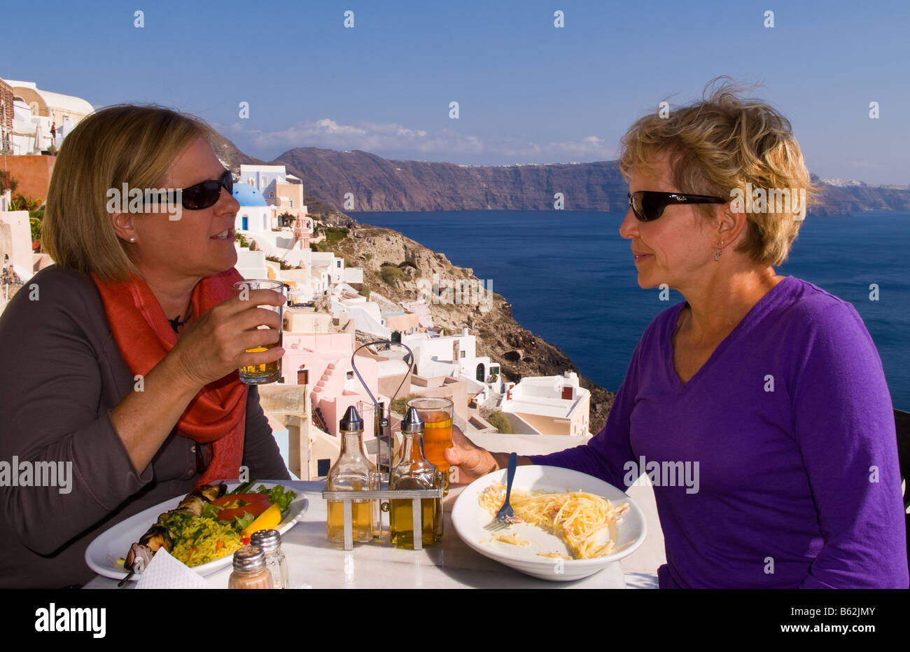 Beau village d'Oia avec de vieux bâtiments blancs comme deux touristes partager un verre en regardant vers le bas dans les îles grecques de Santorin Banque D'Images