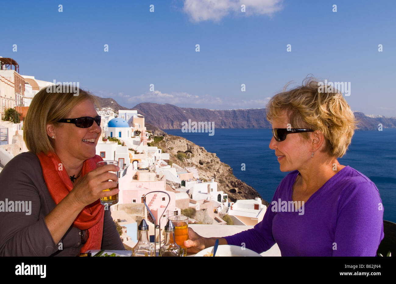 Beau village d'Oia avec de vieux bâtiments blancs comme deux touristes partager un verre en regardant vers le bas dans les îles grecques de Santorin Banque D'Images