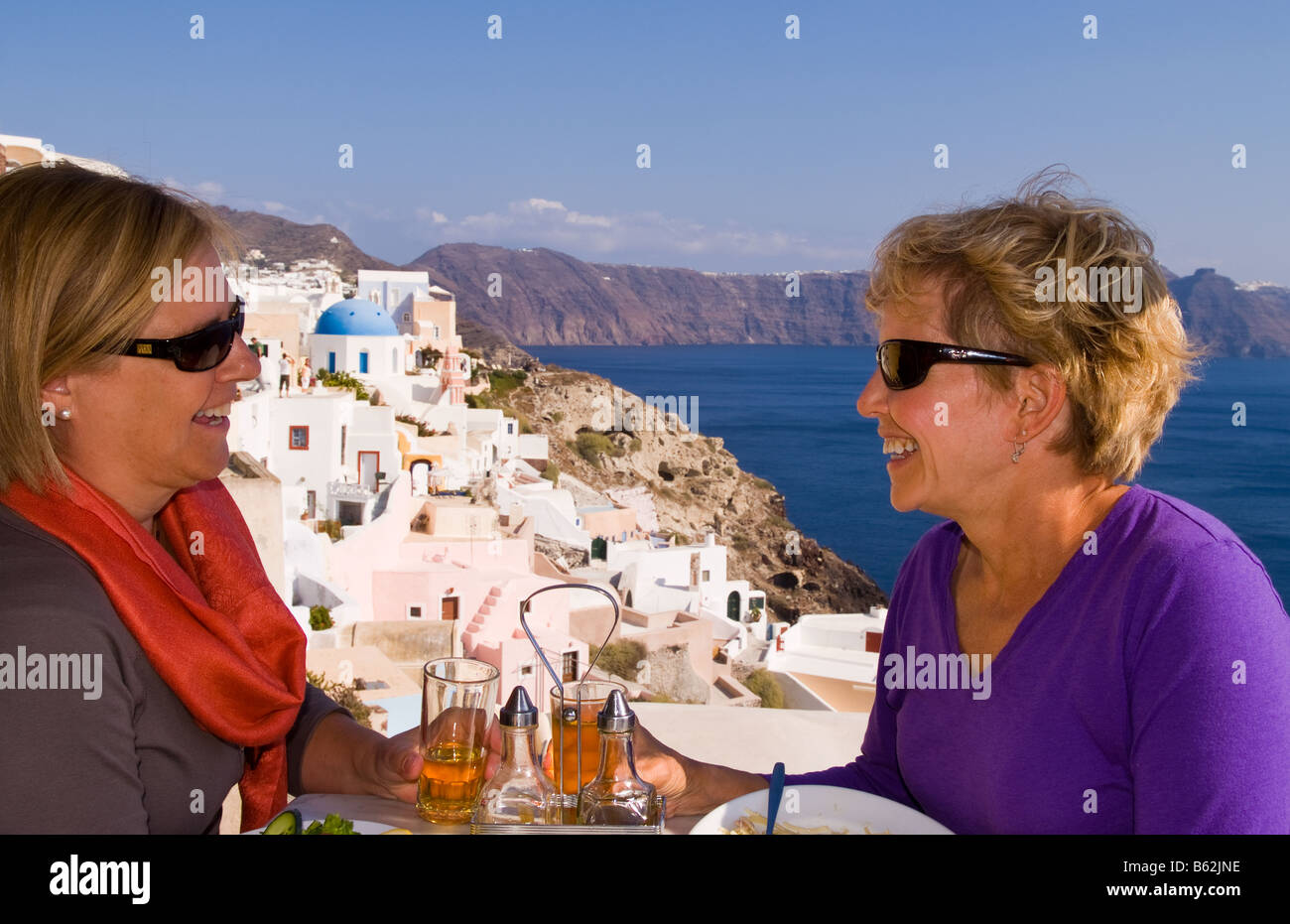 Beau village d'Oia avec de vieux bâtiments blancs comme deux touristes partager un verre en regardant vers le bas dans les îles grecques de Santorin Banque D'Images