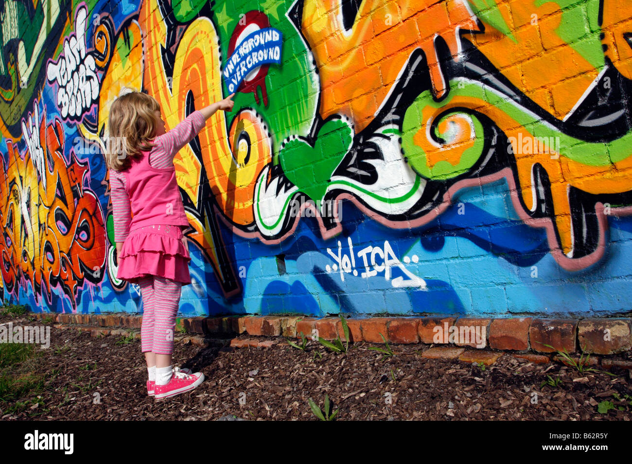 Girl standing by et pointant sur un mur de graffiti wallart dans le cadre d'un projet communautaire de pulvérisation de peinture peinture brique trajet train Banque D'Images
