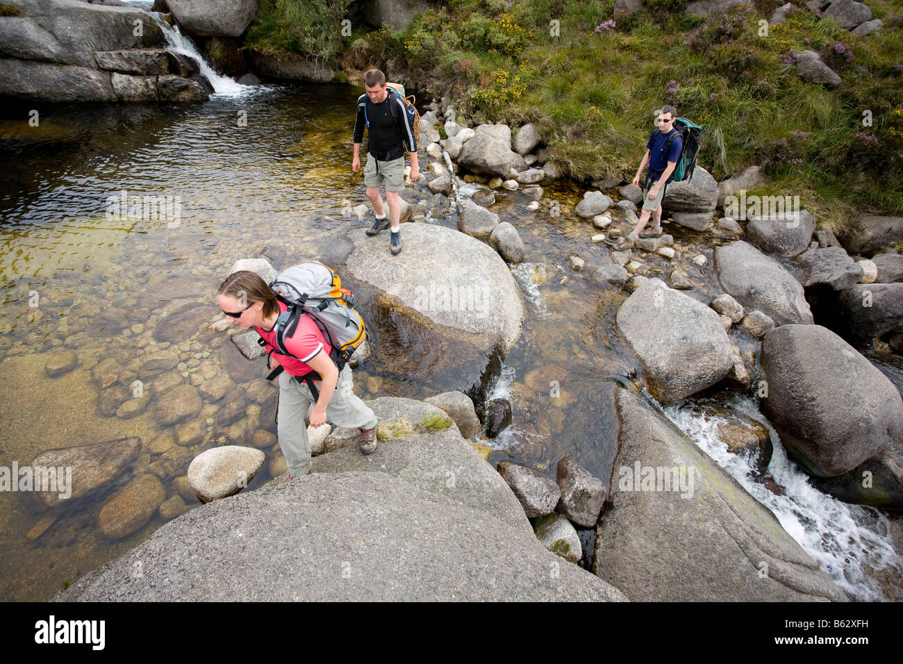 Les randonneurs traversant un ruisseau dans la vallée, les montagnes de Mourne Annalong, comté de Down, Irlande du Nord, Royaume-Uni. Banque D'Images