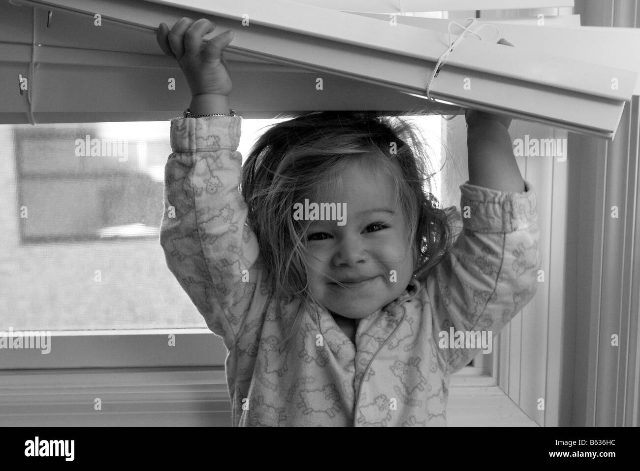 Portrait of a baby girl holding blinds and smiling Banque D'Images