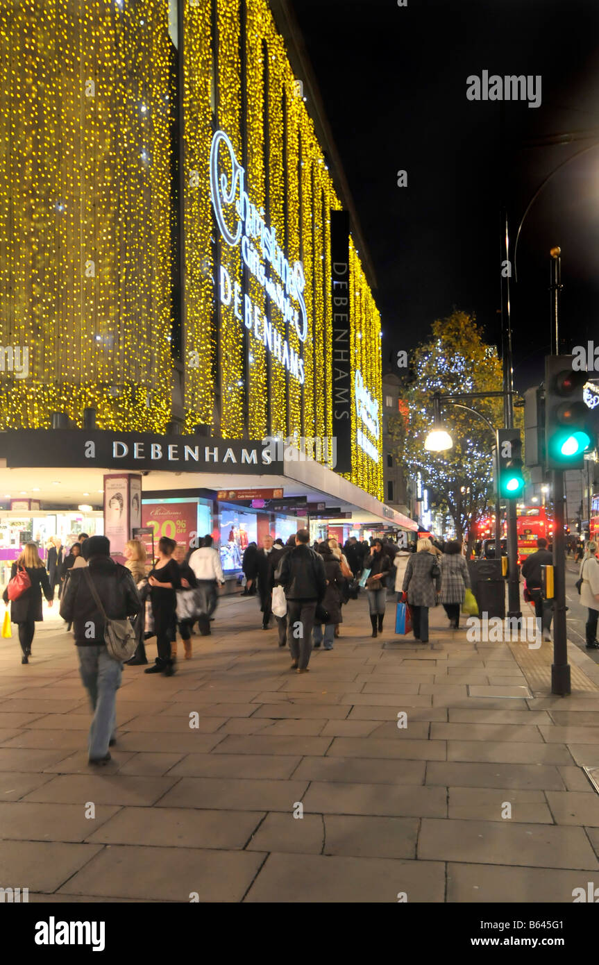 Oxford Street West End Londres Angleterre Royaume-Uni soir Xmas shoppers marchant sur le trottoir à l'extérieur du grand magasin Debenhams avec des décorations de Noël lumière Banque D'Images