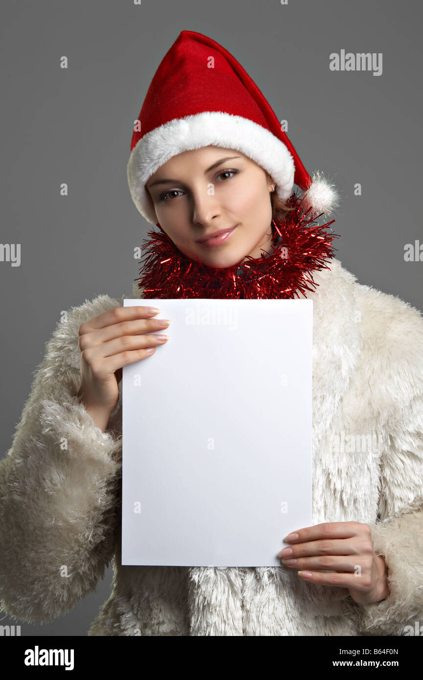 Belle jeune femme en blanc manteau de fourrure et red hat avec feuille de papier sur l'arrière-plan gris Banque D'Images