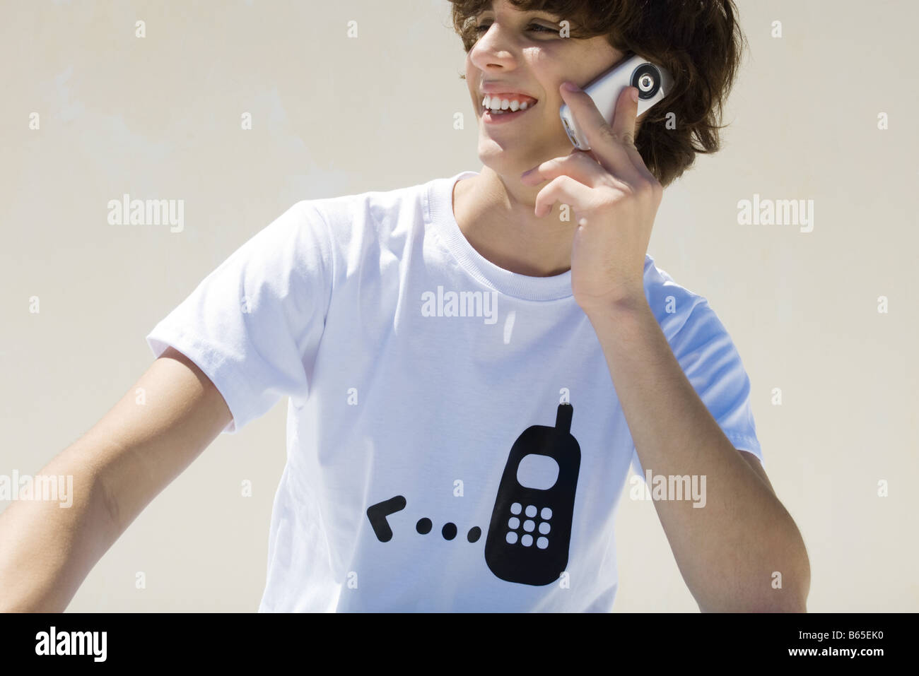 Teenage boy wearing tee-shirt imprimé avec le téléphone cellulaire, à l'aide graphique cell phone, smiling Banque D'Images
