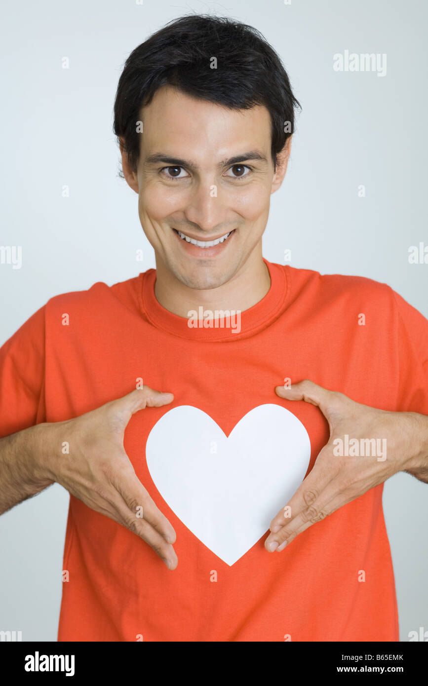 L'homme se tenant la main autour du symbole du cœur imprimé sur son tee-shirt, smiling at camera Banque D'Images