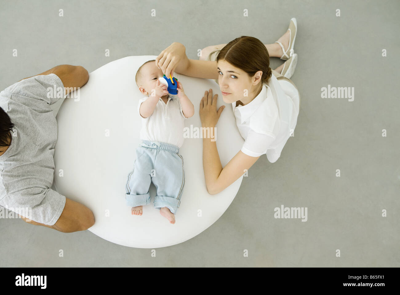 Mère jouer avec bébé couché sur un pouf, père assis avec dos tourné à eux, overhead view Banque D'Images