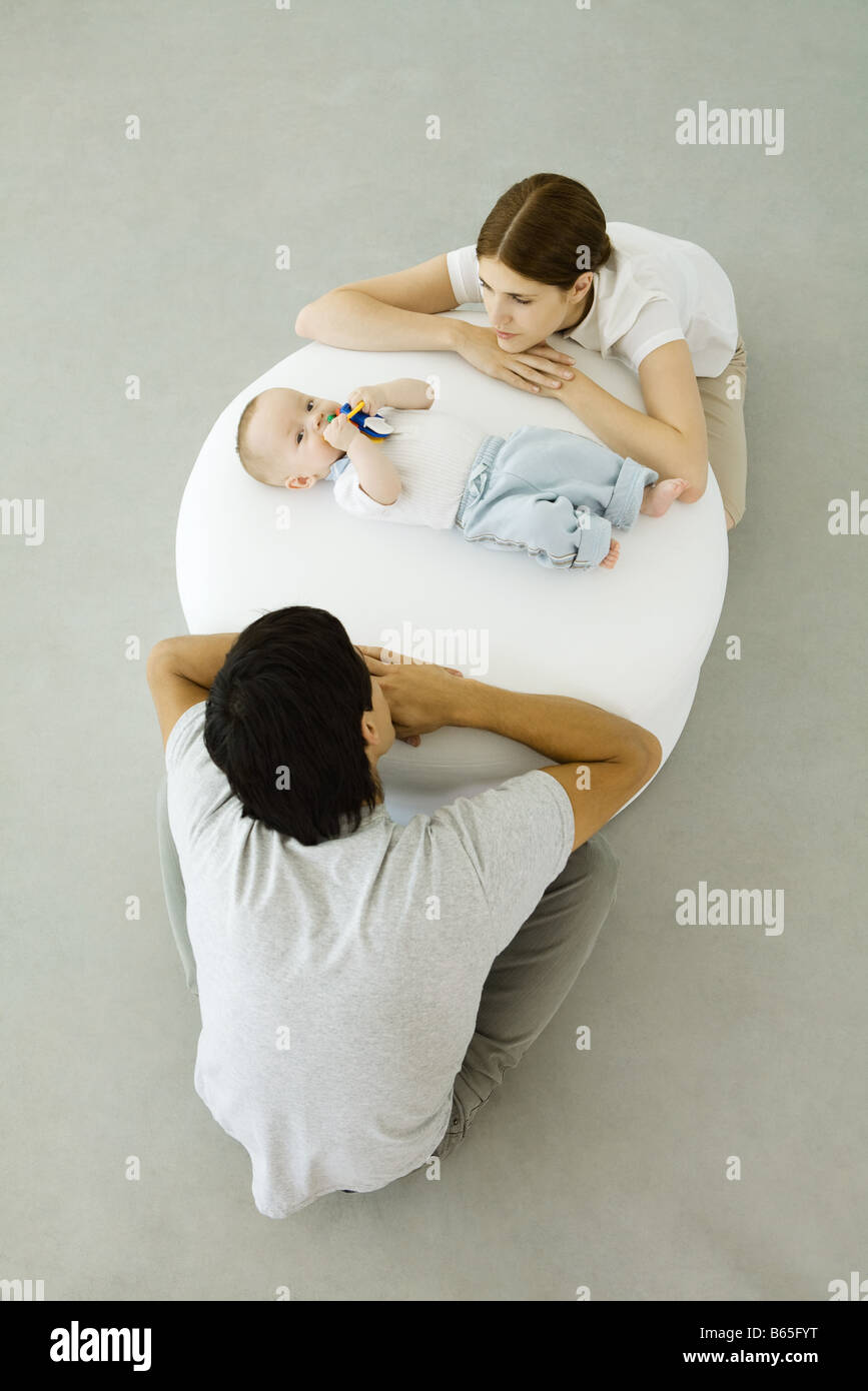 Les jeunes parents appuyé contre un pouf, regardant bébé couché entre eux Banque D'Images