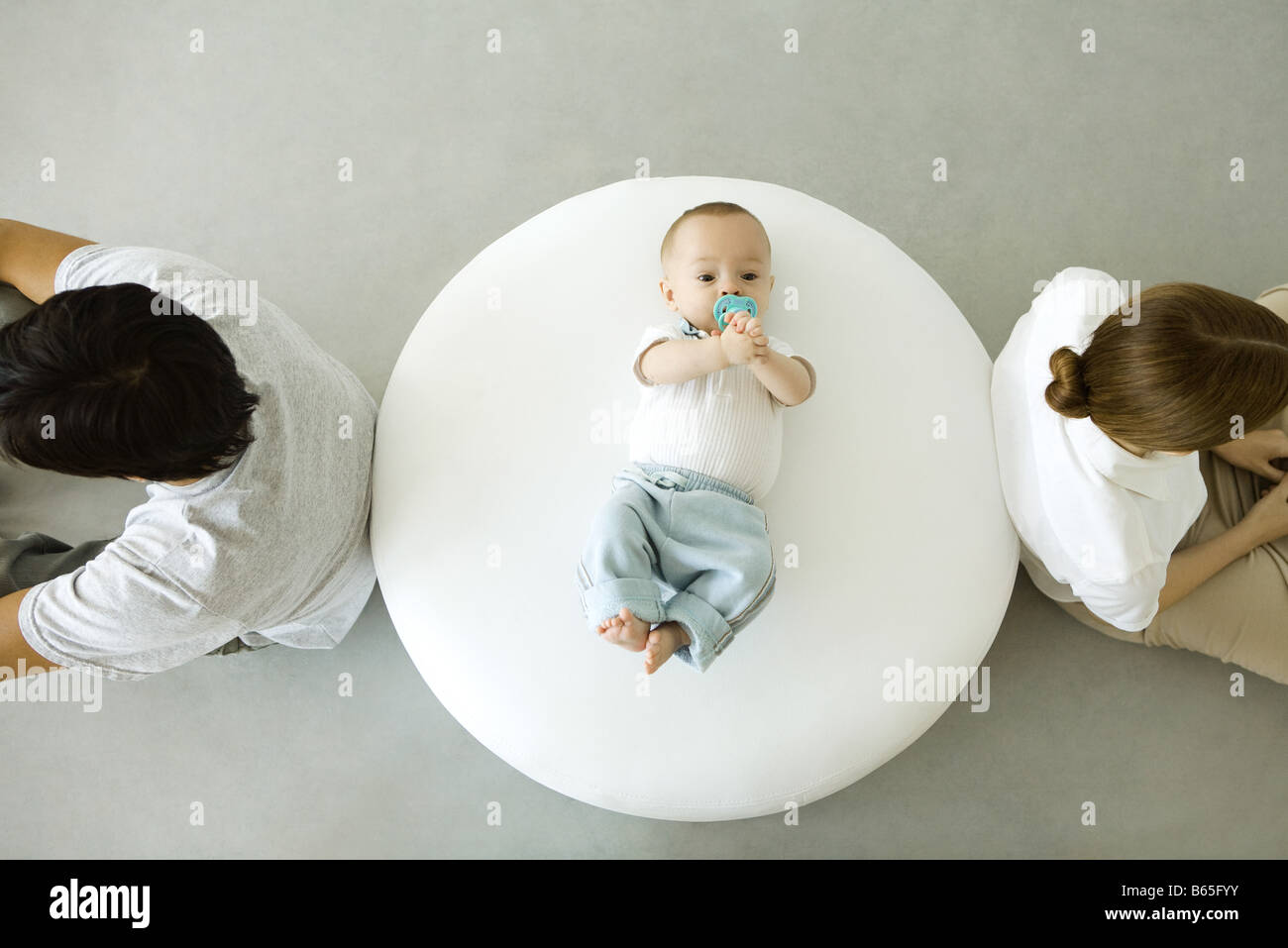 Bébé couché sur un pouf, mère et père assis avec dos tourné, overhead view Banque D'Images