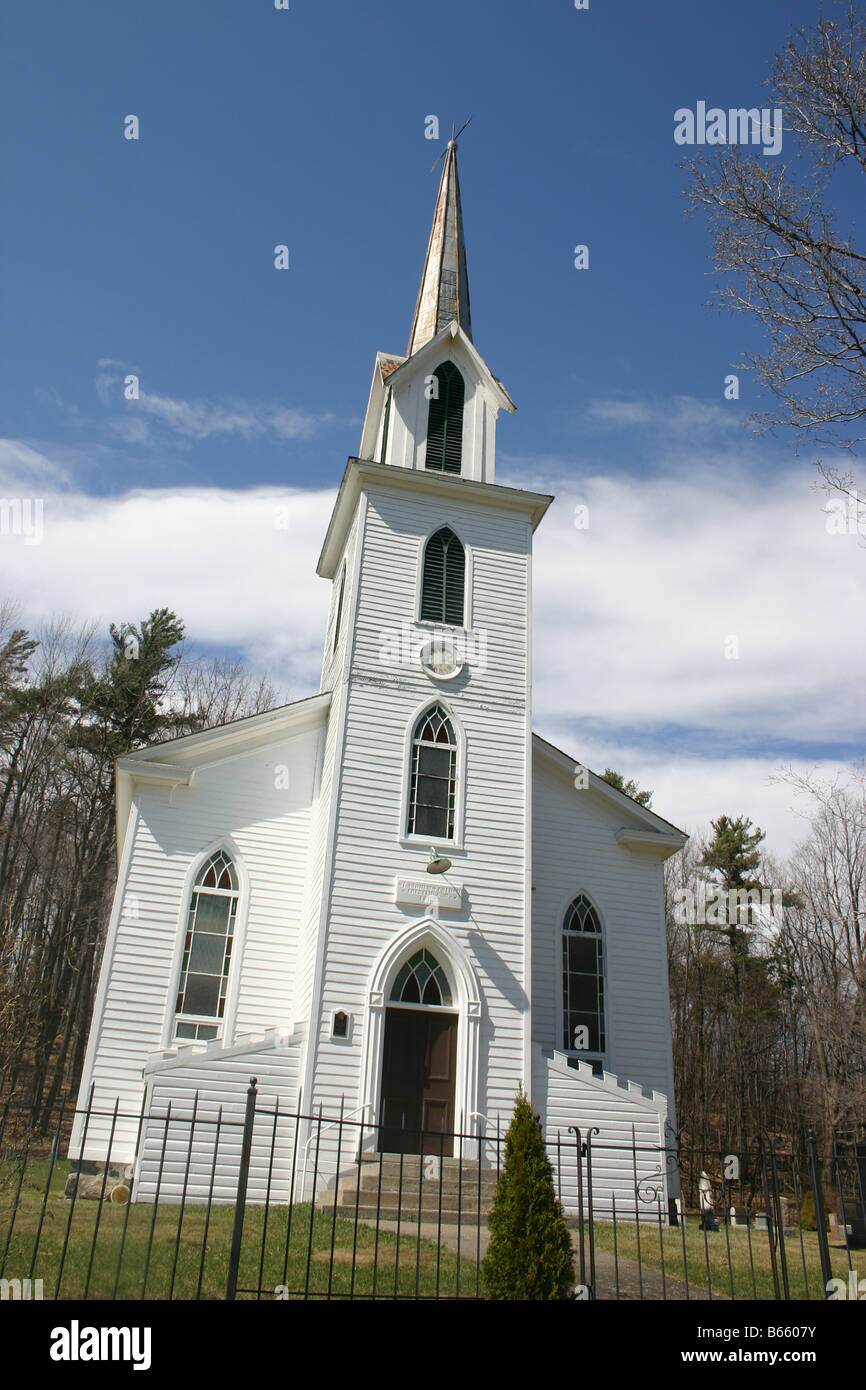 Un petit clin en bois, blanc, église, avec un clocher pointu, entourée d'un petit cimetière et clôture en fer forgé. Banque D'Images