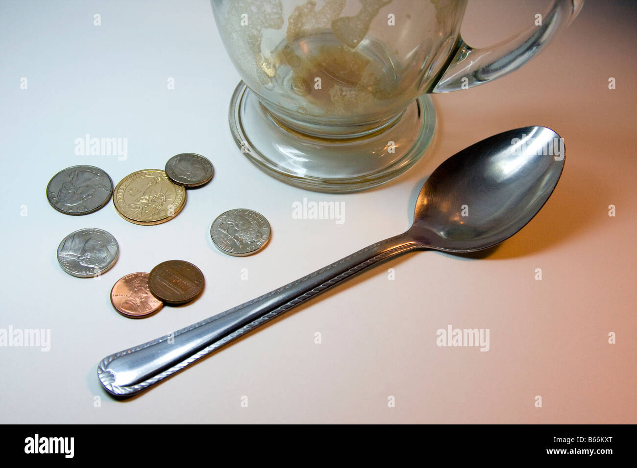 Cappuccino vide le verre, une cuillère de métal sur une surface blanche avec des pièces de monnaie ; 2 pièces, 2 de 5 cents, 1 pièce, 1 trimestre, 1 pièce d'un dollar Banque D'Images