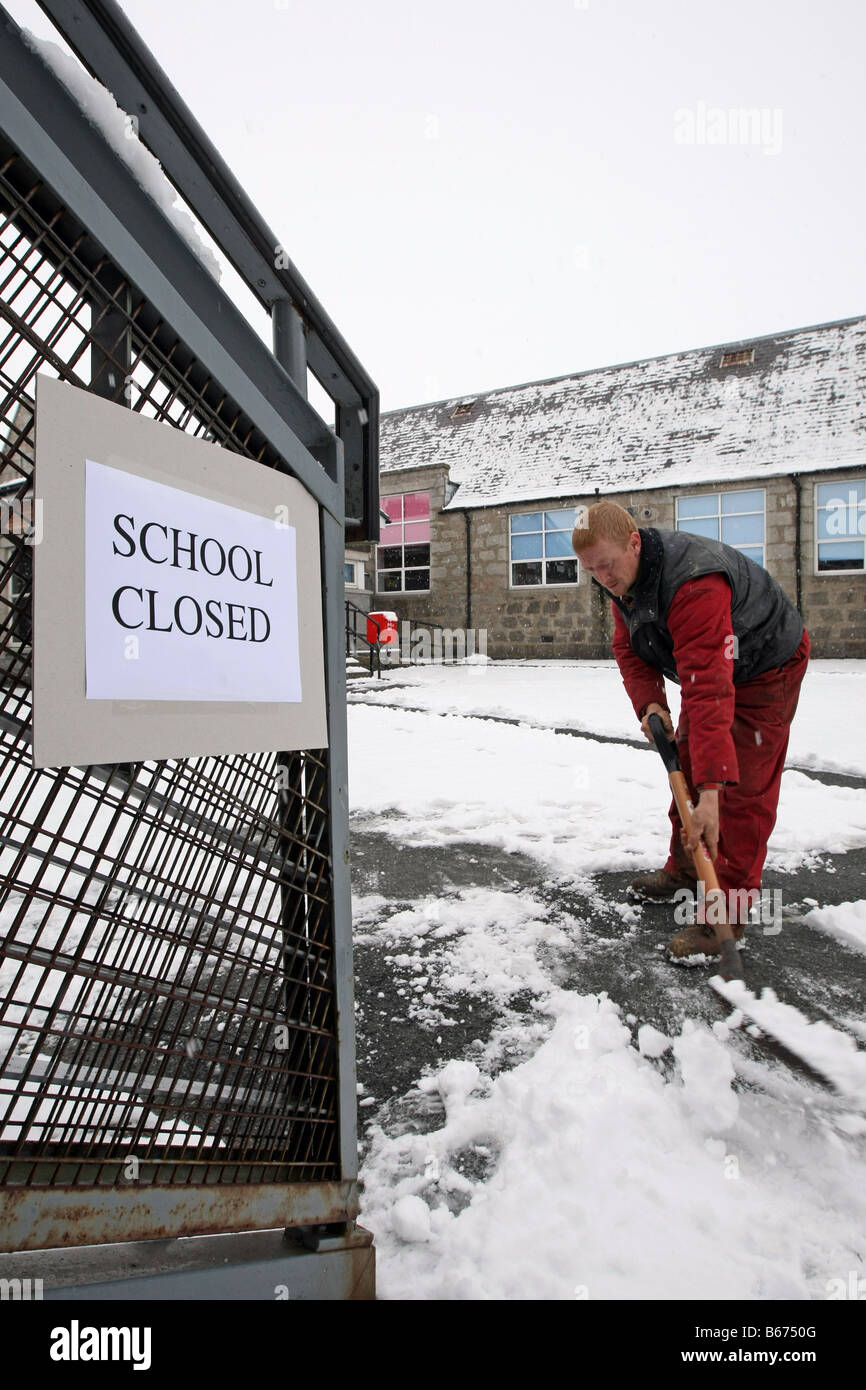 Avec pelle travailleur efface en dehors des chemins d'une école qui est fermée en raison de la neige en hiver, dans l'Aberdeenshire, Ecosse, Royaume-Uni Banque D'Images