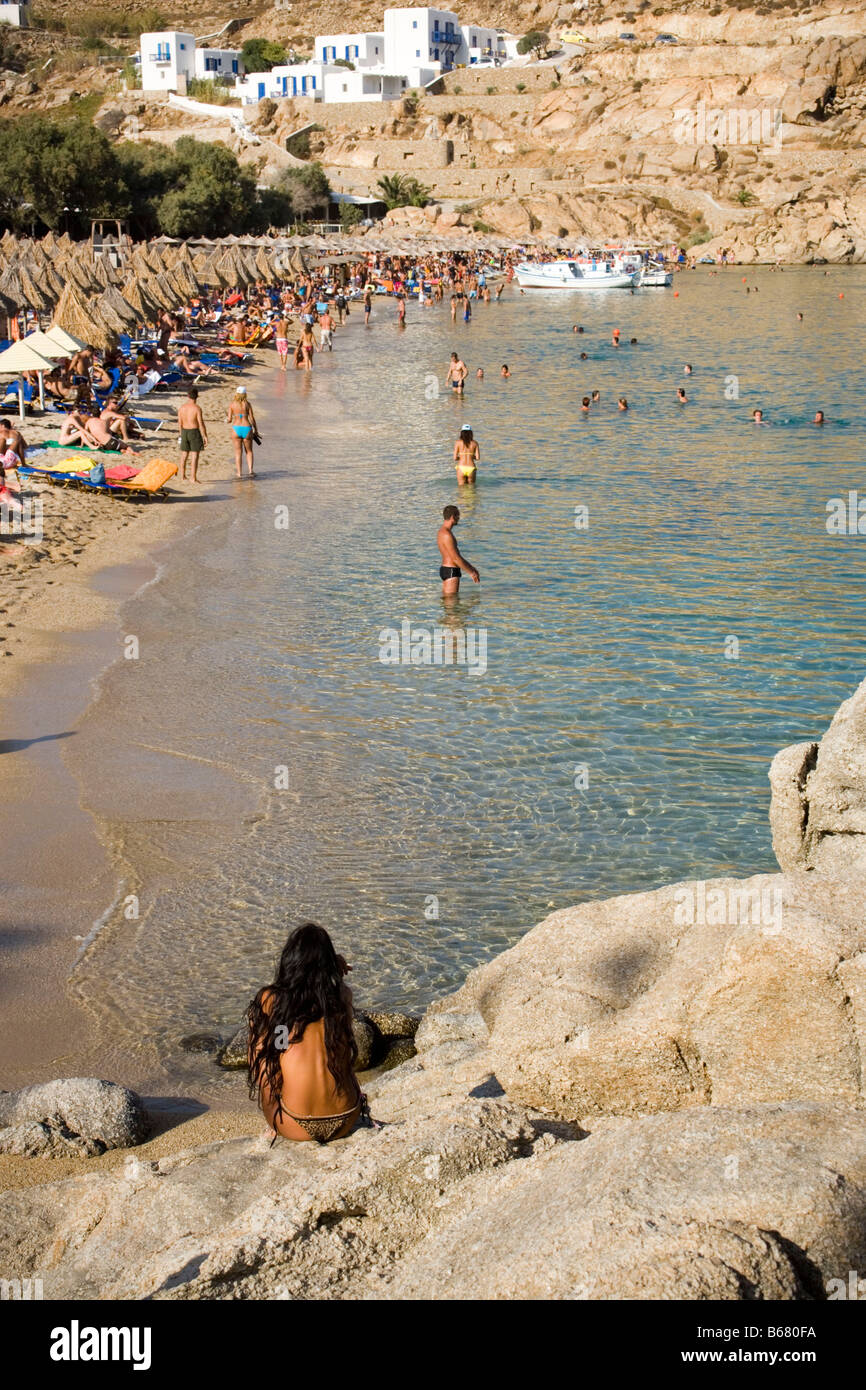 Vue d'une femme assise sur un rocher à la baignade de personnes de Super Paradise Beach, sachant qu'un centrum de gais et de naturisme, Psarou, Banque D'Images