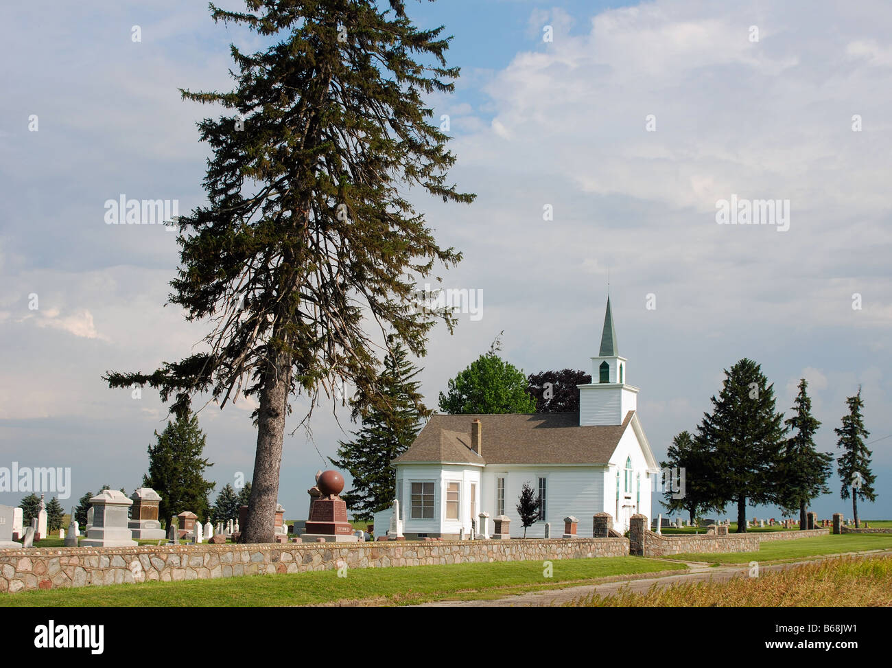 Petite église de campagne avec une flèche verte à côté d'un cimetière Banque D'Images