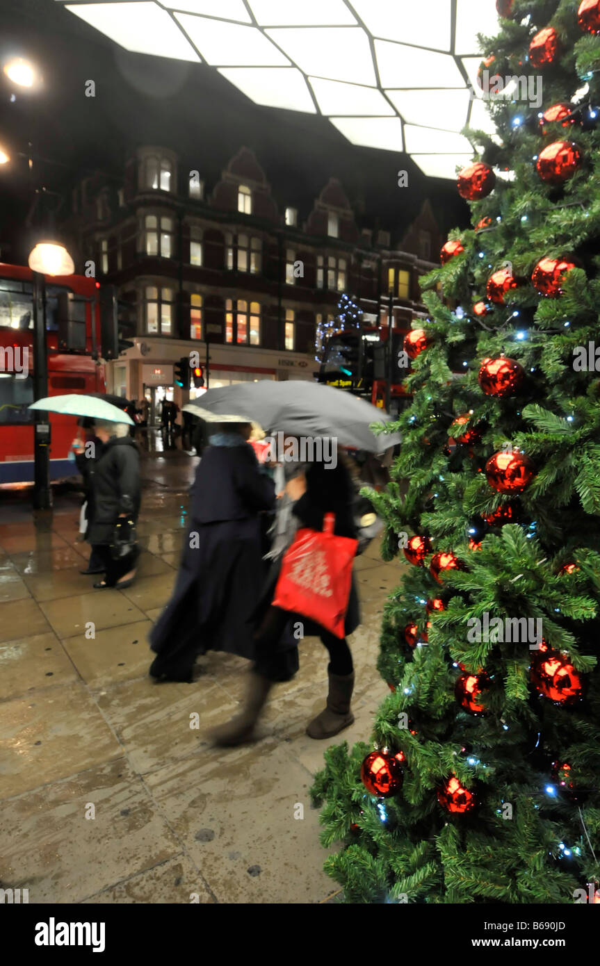 Parasols et arbre de Noël sous la voûte d'entrée éclairée à Grand magasin Selfridges par temps de pluie Oxford Street West Fin Londres Angleterre Royaume-Uni Banque D'Images