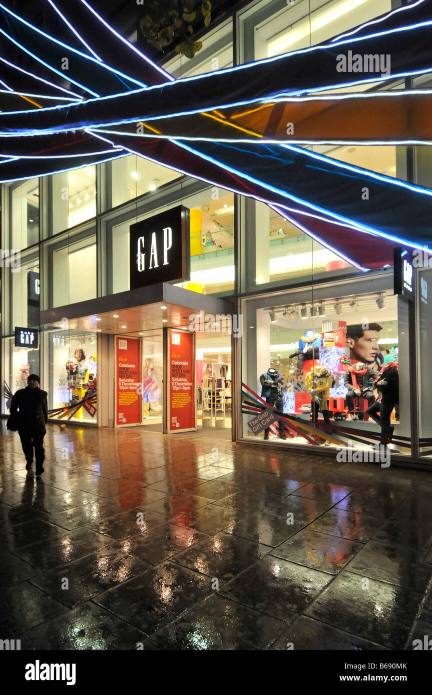 Des clients mouillés à l'extérieur de la boutique de vêtements Gap et de la fenêtre avant de la boutique Oxford Street London West End à la nuit les gens Noël shopping Sous la pluie Angleterre Royaume-Uni Banque D'Images