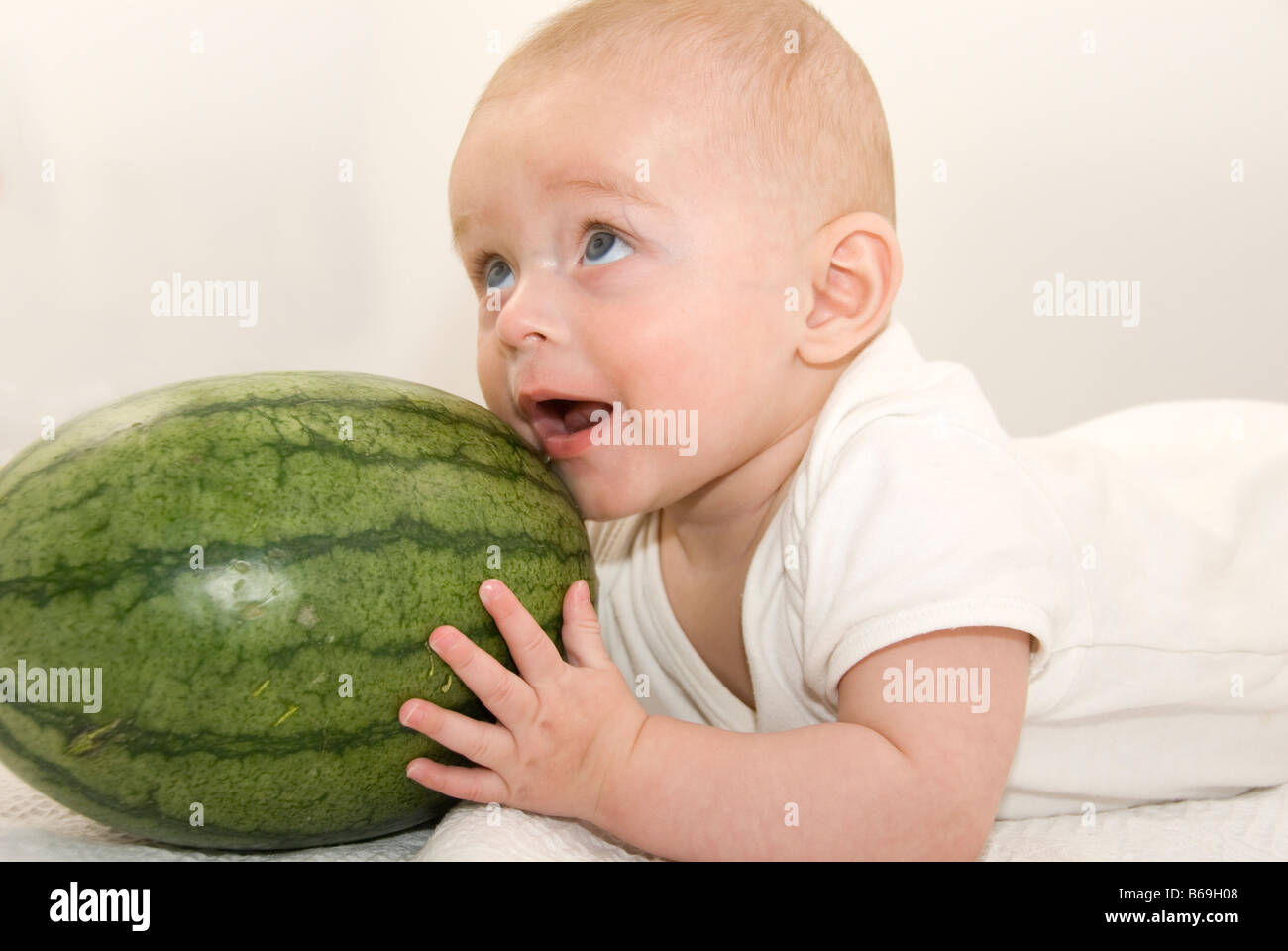 Bébé garçon couché sur le ventre en essayant de manger une énorme pastèque verte Cut Out on White Banque D'Images